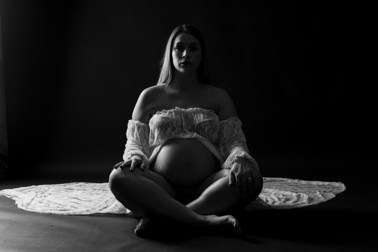 Futura mamma seduta a gambe incrociate con abito in pizzo bianco